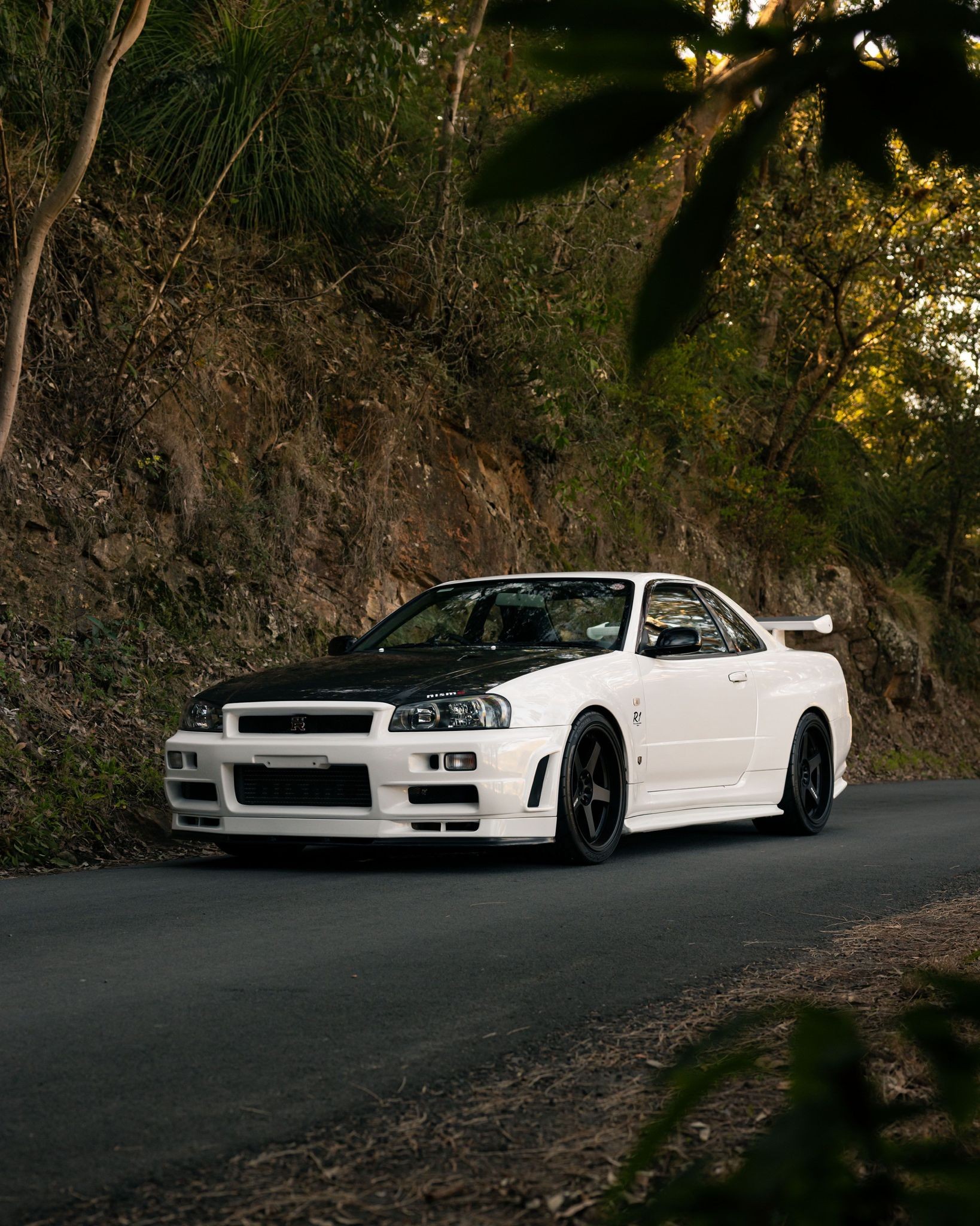White BNR34 NISMO R1 on a mountain road at golden hour